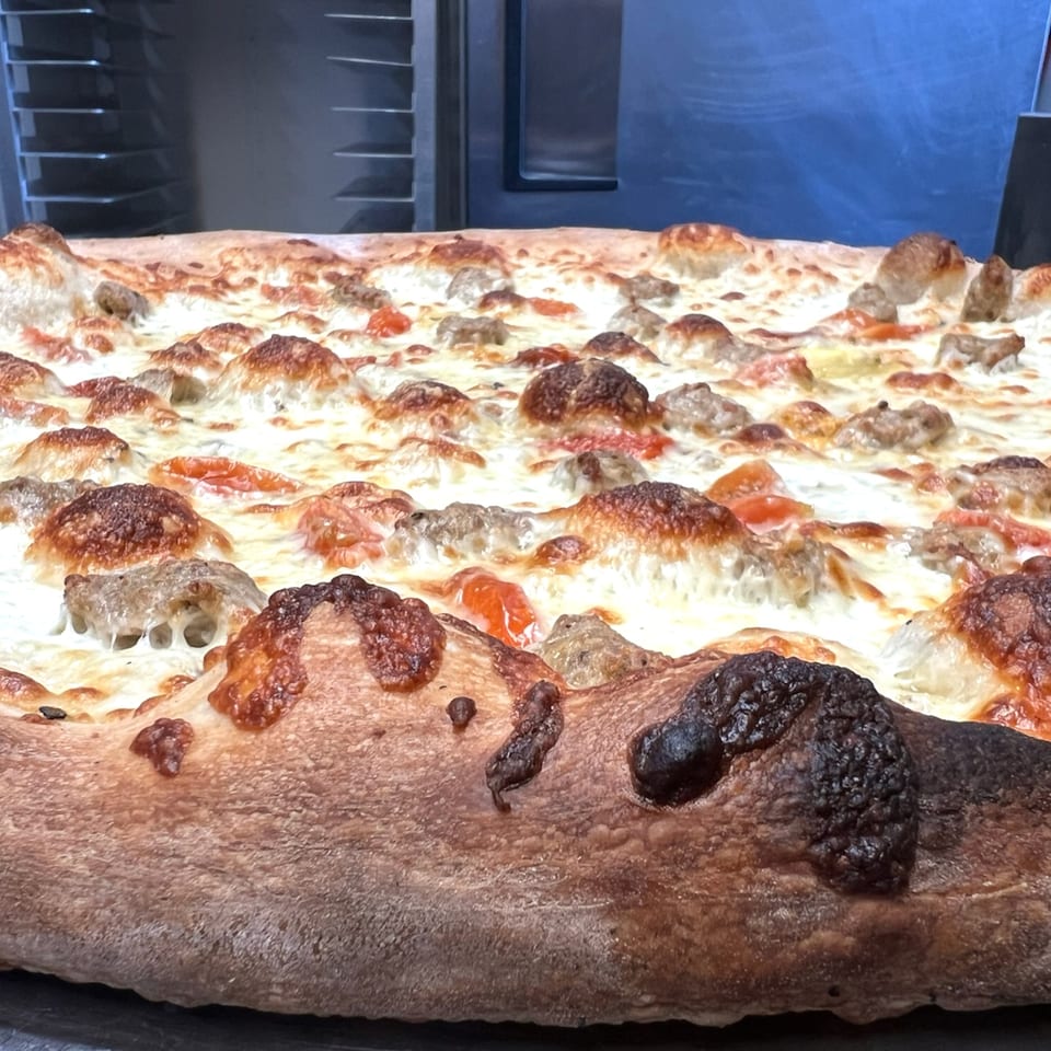 Close-up of a freshly baked Angolino Pizza with melted cheese, sausage, and a crispy crust.