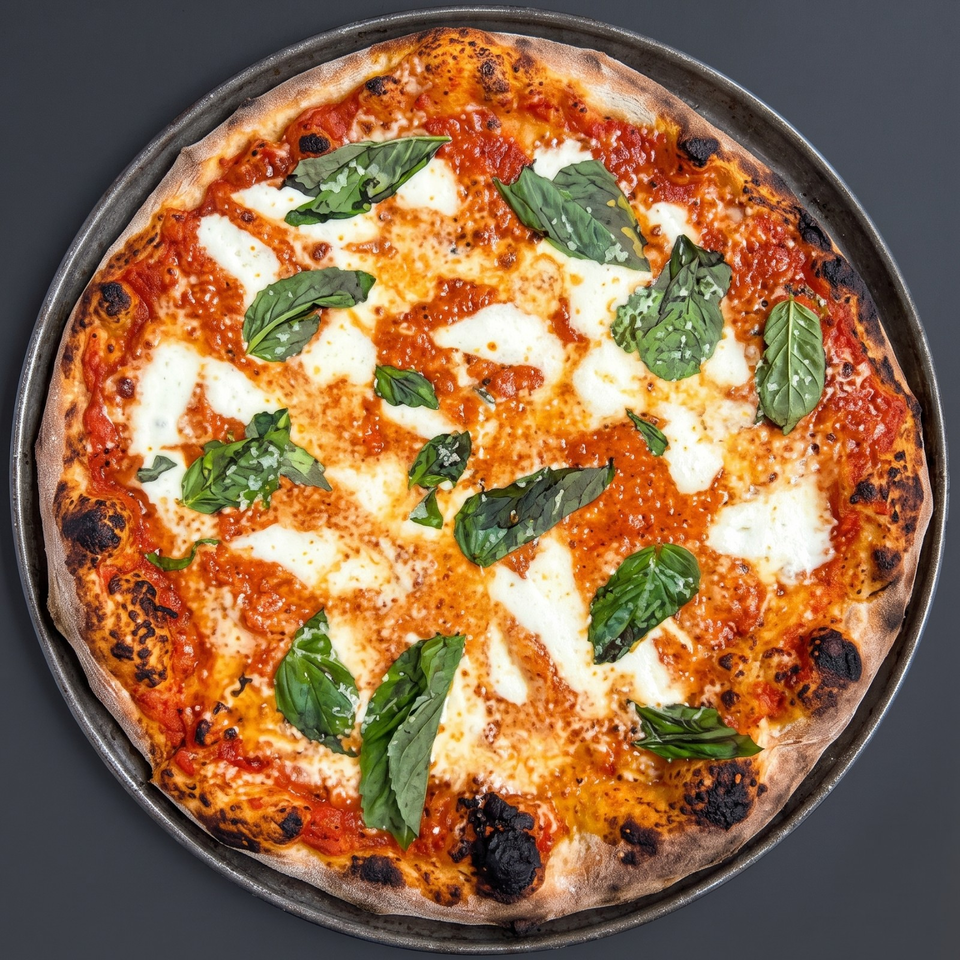 Neapolitan-style Margherita pizza with tomato sauce, melted mozzarella, fresh basil, and charred crust on a dark metal pan.